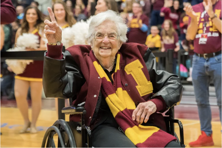 Photo of Sister Jean from Loyola University sitting on the sidelines holding her right hand up to say "#1"